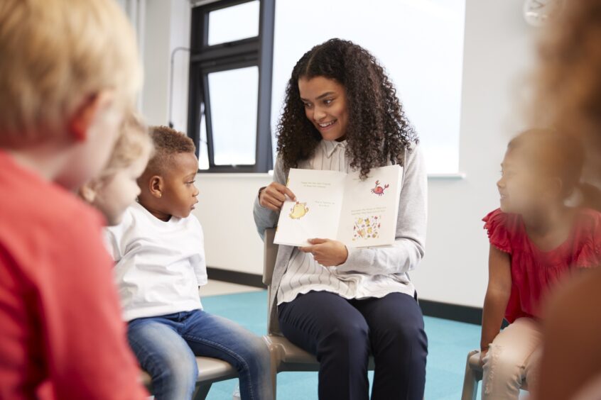 Young woman showing a children's book to school-age kids