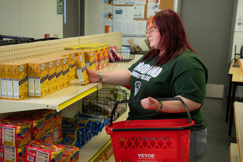 Student at Lake County Campus selecting from pasta, ramen and other food items from the on-campus food pantry
